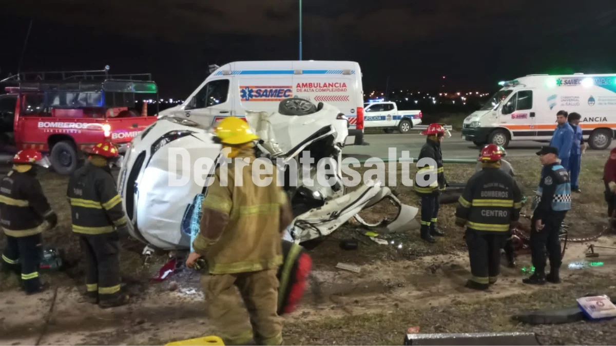 Personal policial y bomberos trabajan junto al vehículo destrozado tras el vuelco en Circunvalación Oeste de Salta.